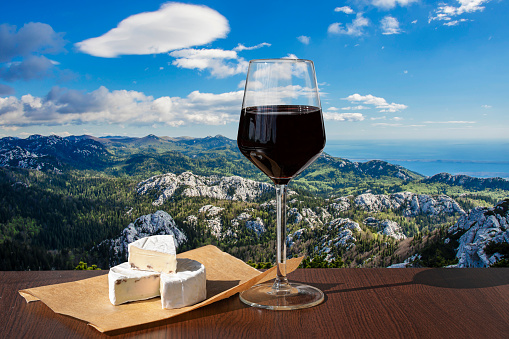 Glass o red wine with brie cheese against beautiful mountain background in Croatia