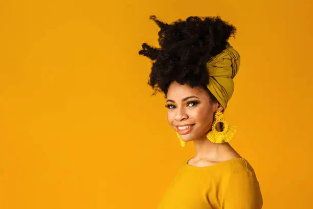 Photo of Portrait of a smiling young woman with big yellow tassel beaded earrings and afro hair wrapped with head wrap scarf