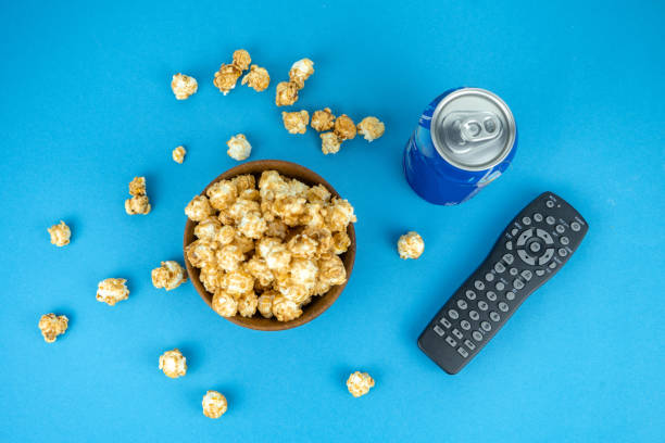 watching movie at home concept, cold refreshing blue pepsi can, wooden bowl of fresh caramel popcorn, remote tv control, top view stock photo