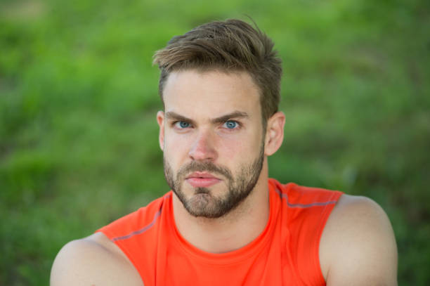 Taking minute break. Runner relaxing in shadow. Man with bristle strict face, grass background. Man unshaven looks handsome and cool. Guy bearded and attractive relaxing at meadow during workout.