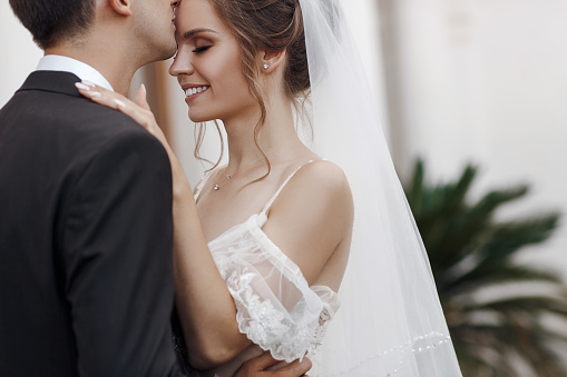 wedding day. beautiful bride in white long dress and young groom wearing in black suit are hugging in historic europe town.