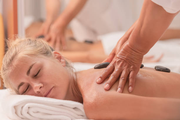 a relaxed looking woman lying down with black stones on her back and receiving a massage from two hands Close up of a relaxed looking woman lying down with black stones on her back and receiving a massage from two hands on an out of focus background. Well-being and leisure concept. reflexology stone massaging human foot stock pictures, royalty-free photos & images