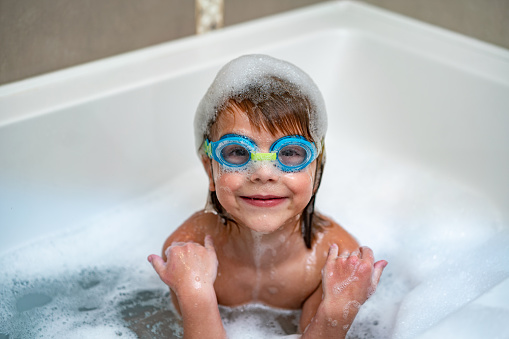 Cute boy is playing in bathtub while wearing swimming goggles