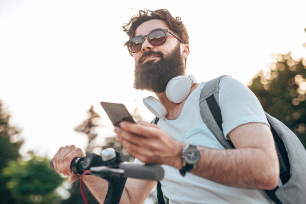 Smiling hipster with gadget riding electric scooter