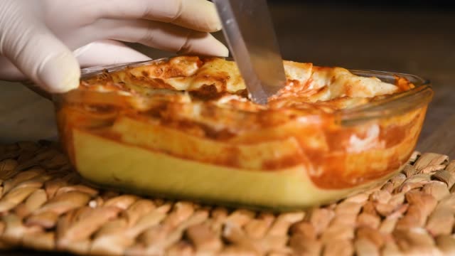 Close up of a delicious looking homemade lasagna being cut repeteadly with the tip of a knife. Homemade food and cooking concept.