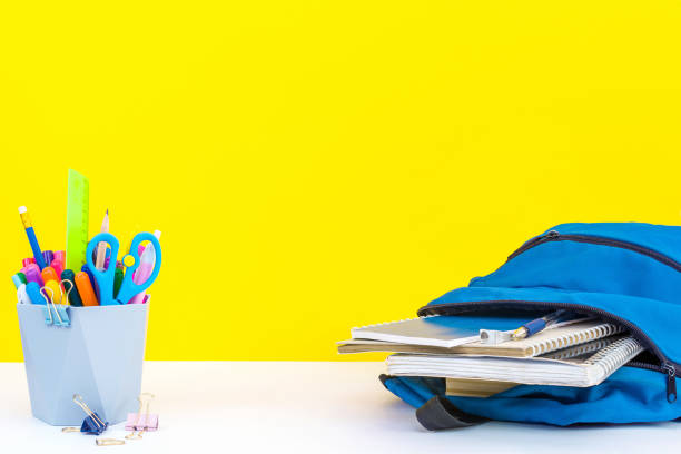 Back to school, education concept, open backpack with notebooks, stationery and organizer with multi-colored pens, pencils and scissors on a white table on a yellow background with copy space. Back to school, education concept, open blue backpack with notebooks, stationery and organizer with multi-colored pens, pencils and scissors on a white table on a yellow background with copy space. classroom empty education desk stock pictures, royalty-free photos & images