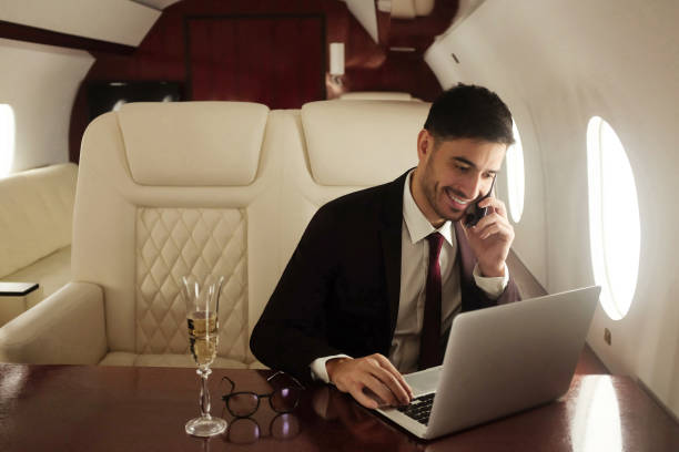 milliardär oder reicher geschäftsmann fliegt erstklassig und arbeitet im flugzeug mit laptop und glas champagner. privatjet - vehicle interior corporate jet jet private airplane stock-fotos und bilder