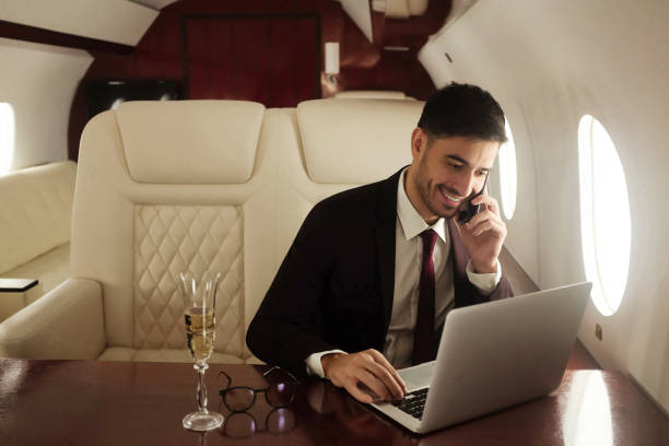 миллиардер или богатый бизнесмен летает первым классом и работает на самолете с ноутбуком и бокалом шампанского. частный самолет - vehicle interior corporate jet jet private airplane стоковые фото и изображения