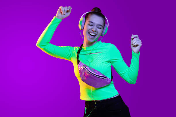 ragazza felice che indossa il top verde e balla musica ascoltando attraverso le cuffie, isolata su sfondo al neon - purple belt foto e immagini stock