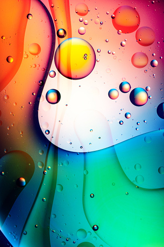 Colourful patterns of oil drops in water against vibrant defocused background extreme close-up