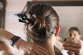 Back view of young attractive woman with hair bun shell-wrapped, with three wooden hairpins of sophisticated shapes. Close up head, hand with black electronic watch on wrist