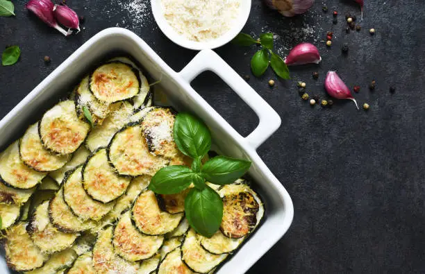 Zucchini casserole with cream, garlic and parmesan on a black background. View from above.