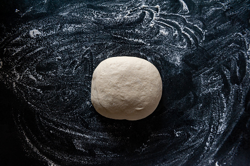 Homemade dough for a Pizza, surrounded by flour on a slate plate.