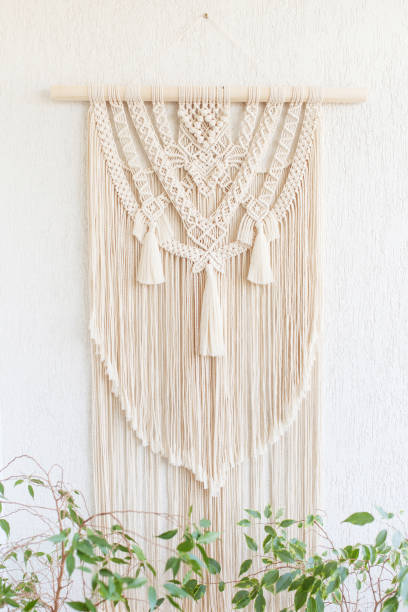 istock Handmade macrame. 100% cotton wall decoration with wooden stick hanging on a white wall.   Macrame braiding and cotton threads.  Female hobby.  ECO friendly modern knitting DIY natural decoration concept in the interior 1255742918