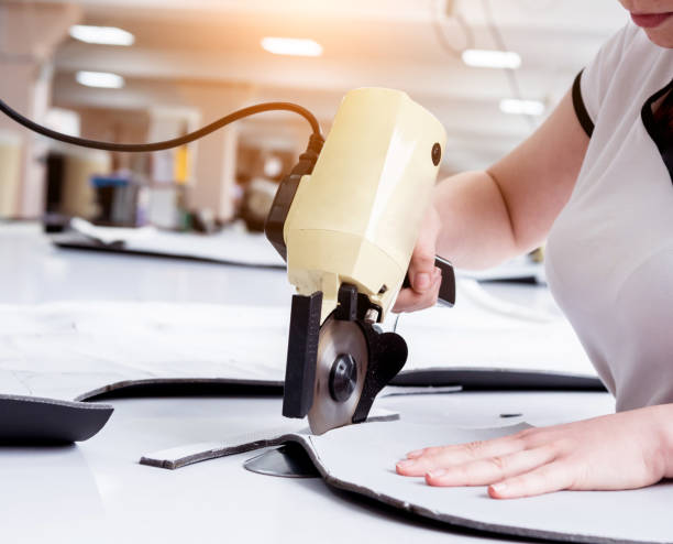 istock Female worker uses electric cutting fabric machine. Fabric industry production 1255743246