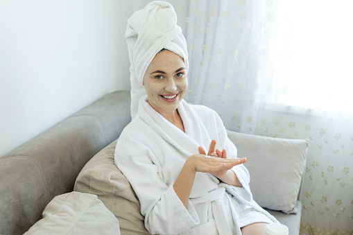 Young woman with towel is applying mask on her face