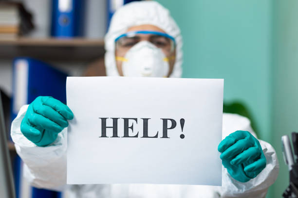 istock Disinfection man with special white suite holding help word at the office 1255745967