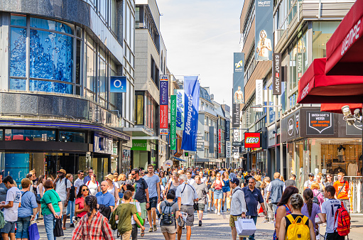 Cologne, Germany, August 23, 2019: crowd of people tourists walking down pedestrian shopping street Hohestrasse with many multibrand stores and shops in historical city centre