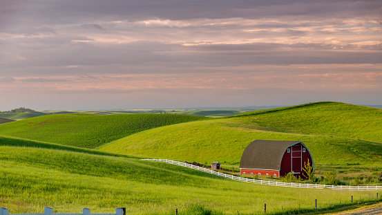 Distant farm fields with a bright red barn and white fence