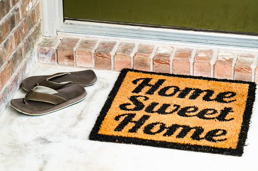 Home Sweet Home doormat and two flip flop sandals left on the front porch in front of the front door of a nice new brick home