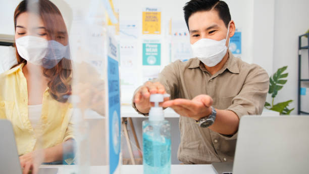 Asian business people wear face mask, wash hand using hand sanitizer, and separated by partition stand. Social distancing at work, new normal office lifestyle after coronavirus lockdown concept Asian business people wear face mask, wash hand using hand sanitizer, and separated by partition stand. Social distancing at work, new normal office lifestyle after coronavirus lockdown concept office cubicle mask stock pictures, royalty-free photos & images