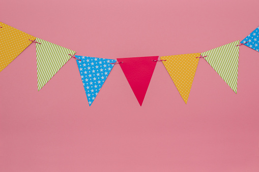 Festive garland of multi-colored paper flags on a pink background. Birthday greeting card with copy space.