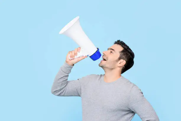 Photo of Caucasian man shouting on megaphone isolated on light blue background