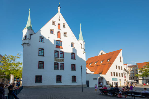 View of historic buildings and a clock tower with colorful shutters under a blue sky in Regensburg, Bavaria, Germany.