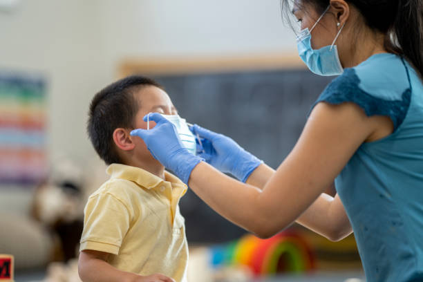 istock Daycare facilitator helping child put on a protective face mask 1255761668
