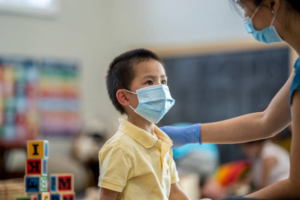 istock Daycare facilitator helping child put on a protective face mask 1255761694