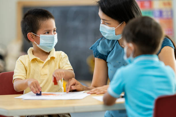 istock Two young boys and a daycare instructor colouring at a table while wearing masks 1255761741