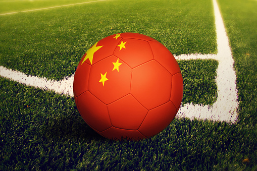 China flag on ball at corner kick position, soccer field background. National football theme on green grass.