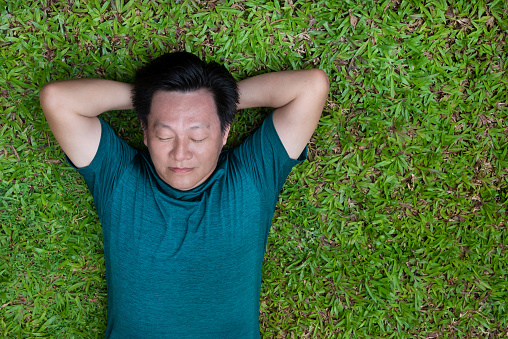 A mid-aged happy adult take a rest on green grass on summer day at public park.