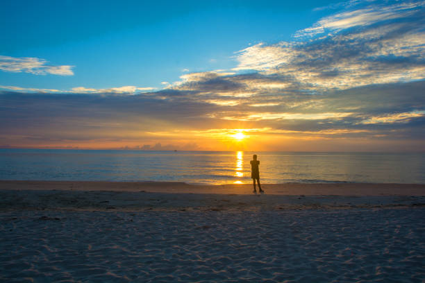 istock Man relaxing on the beach at sunrise, beautiful cloudy sky 1255765570