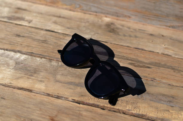 черные солнцезащитные очки лежат на солнце на деревянном фоне - sunglasses wood black dark стоковые фото и изображения