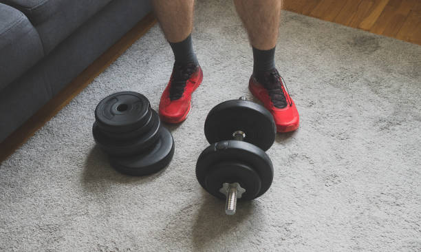 Man standing near adjustable dumbbell with plates at home. Man standing near adjustable dumbbell with plates at home. adjustable stock pictures, royalty-free photos & images