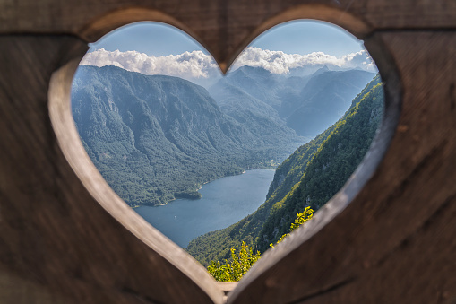 High angle view through heart shape opening of famous viewpoint on panorama Lake Bohinj and the mountains around.