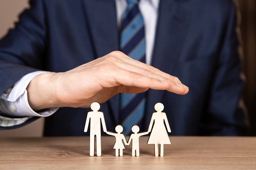 A man in a suit holds hands in the shape of a house over the family. Insurance concept.