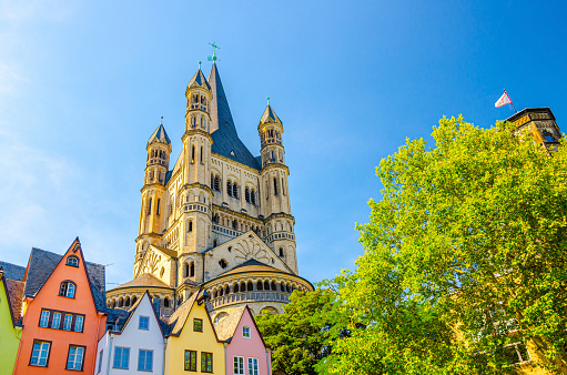 Tower with spire of Great Saint Martin Roman Catholic Church Romanesque architecture style building with green trees and row buildings foreground, blue clear sky, North Rhine-Westphalia, Germany