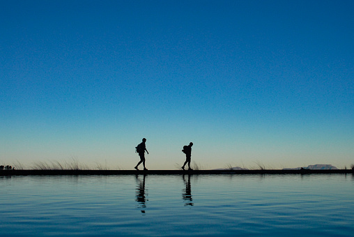 Silhouette Hikers walking together on lake shore reflection with blue clear sky
