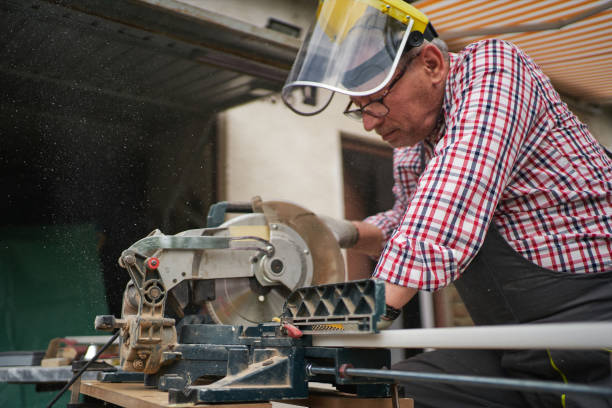istock Senior carpenter with a protective visor cutting a plank with a saw 1255785911
