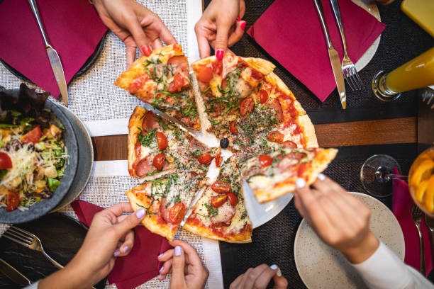 Food is like your story, you can only share it with your best friends Group of people enjoying perfectly made italian pizza cut in pieces and set on dining table in restaurant Ready To Eat stock pictures, royalty-free photos & images