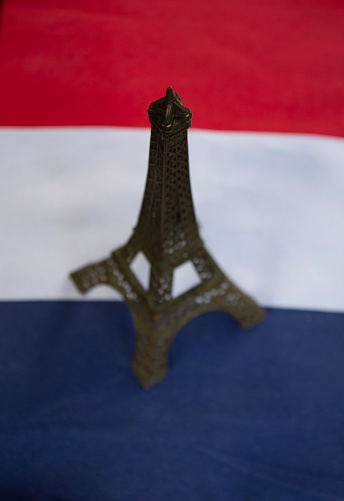 Focus on tip of mini metal Eiffel Tower from Paris on blurred red white blue flag celebrating Bastille day 14th of July French revolution