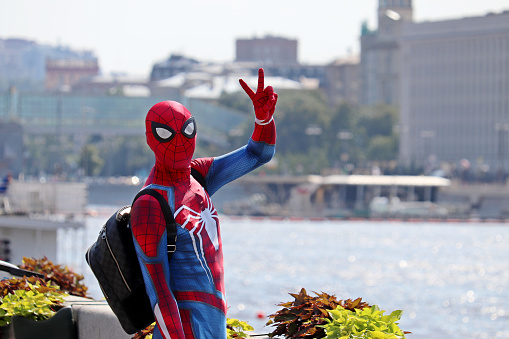 Moscow, Russia - July 2020: Person in Spider-man costume shows the victory sign on Moscow river embankment. Cosplayer in a summer city, entertainment and hobby