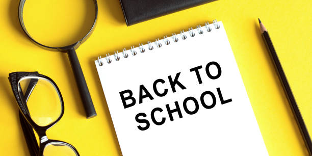 istock Back to school concept. Post it notebook with text back to school and glasses, magnifier andn pensil on yellow background. Flat lay, top view. 1255788205
