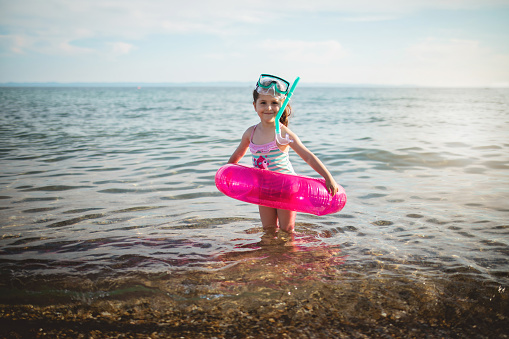 Excited girl with a scuba mask and inflatable ring having fun at the beach holiday