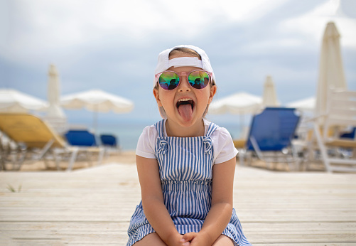 Playful cute little girl sticking out tongue while relaxing at the beach