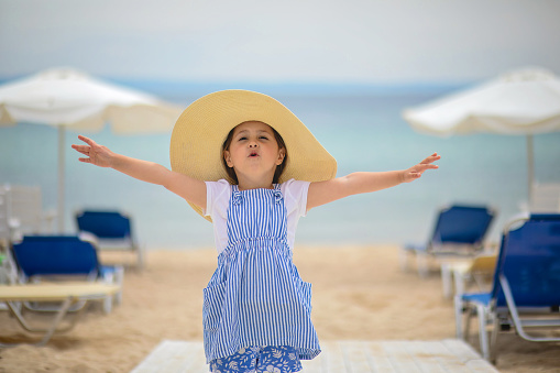 Excited and happy little girl in a dress and sun hat enjoying her family vacation