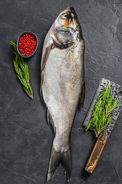 istock Raw whole fish silver carp with pink pepper and rosemary. Black background. Top view 1255789525