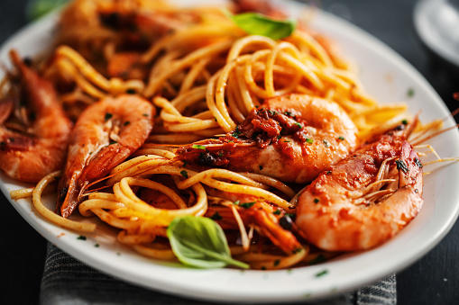 Pasta spaghetti with shrimps and tomato sauce served on plate on dark background.